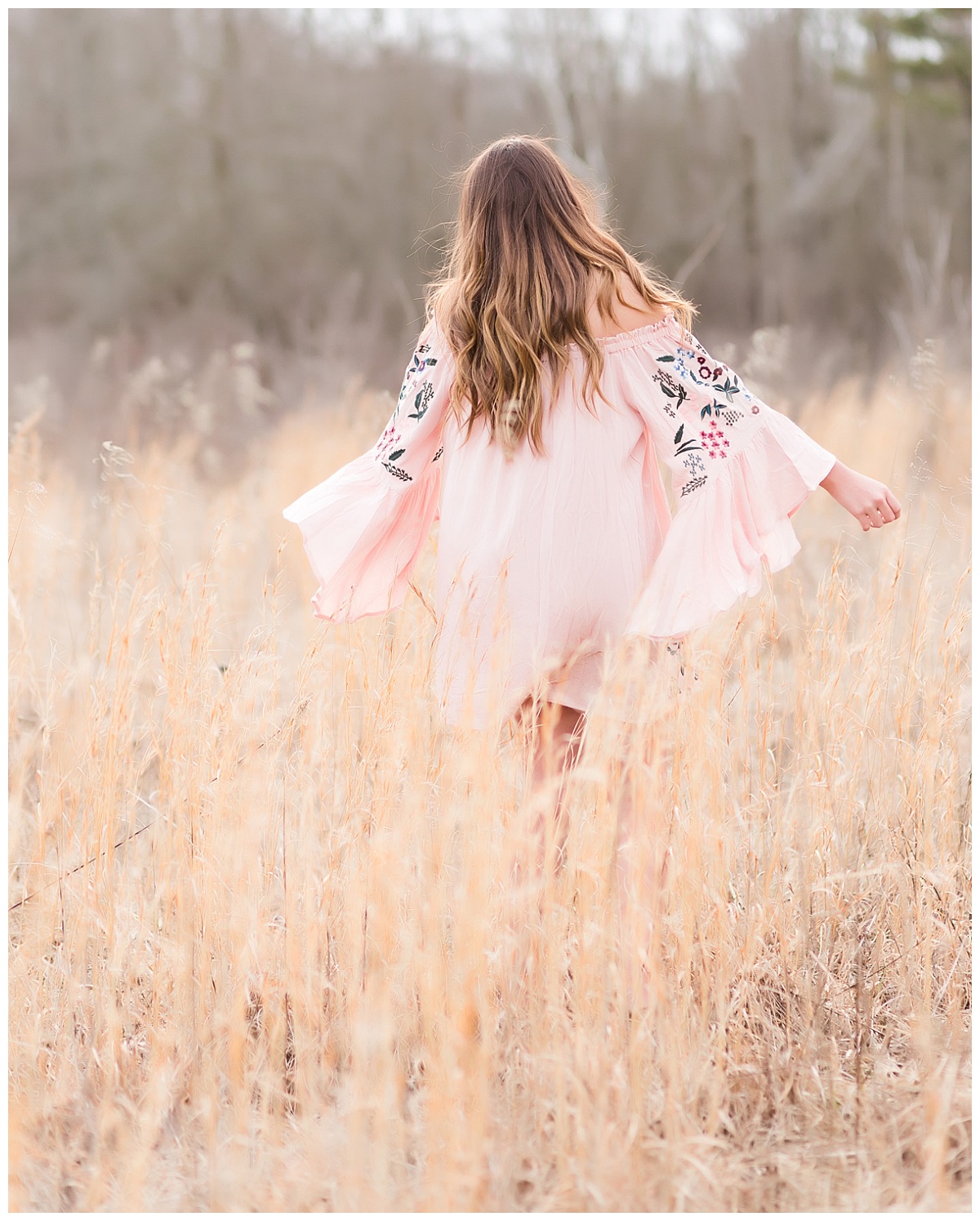 Senior girl in pink dress twirling in field of tall grass