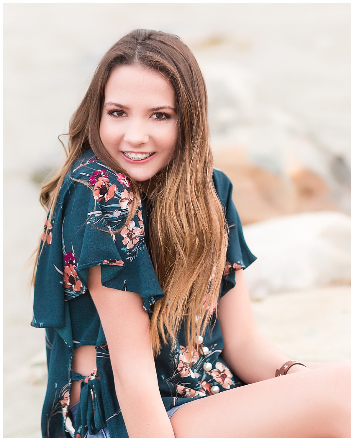 senior girl smiling sitting on rocks near beach 
