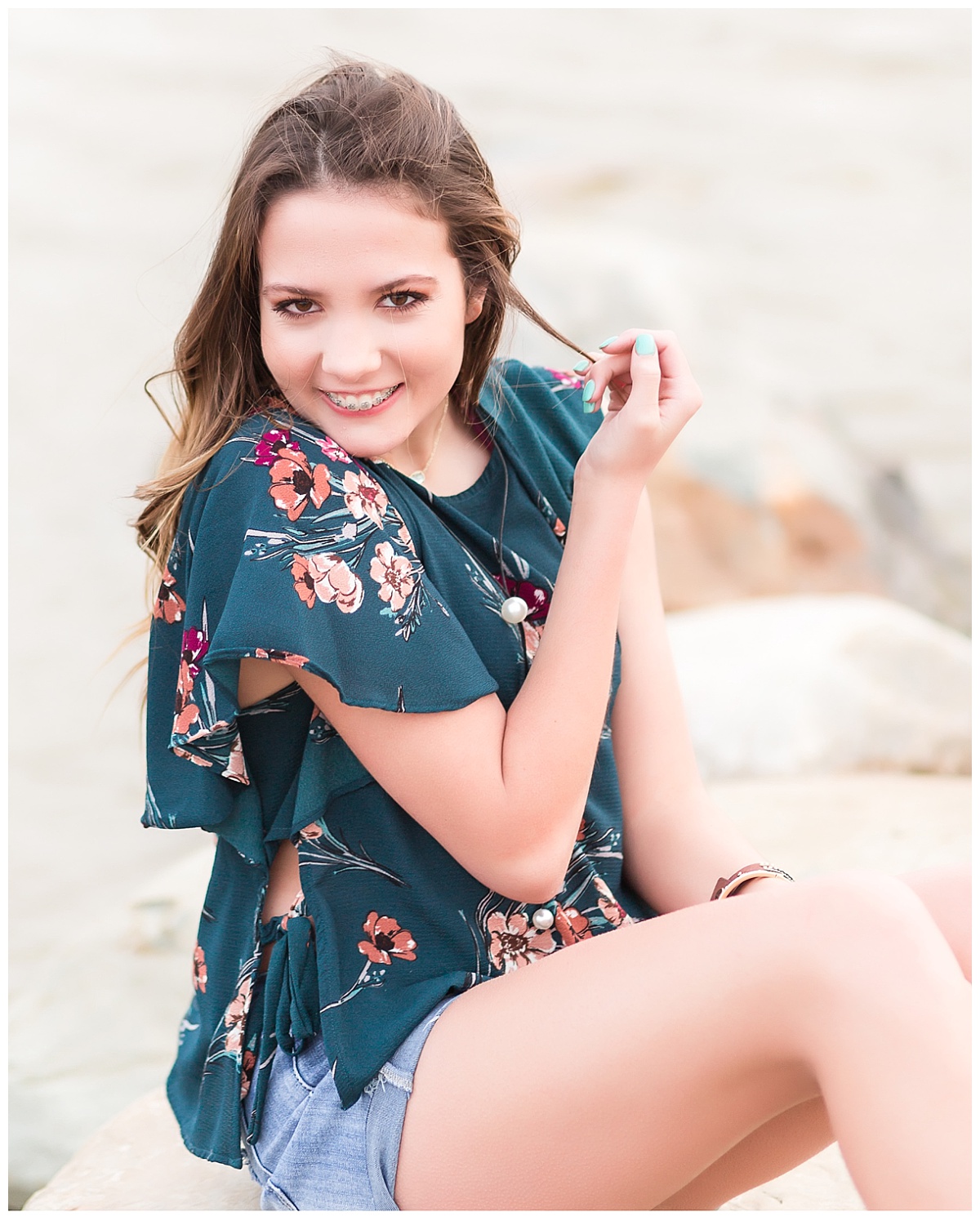 senior girl smiling sitting on rocks near beach 
