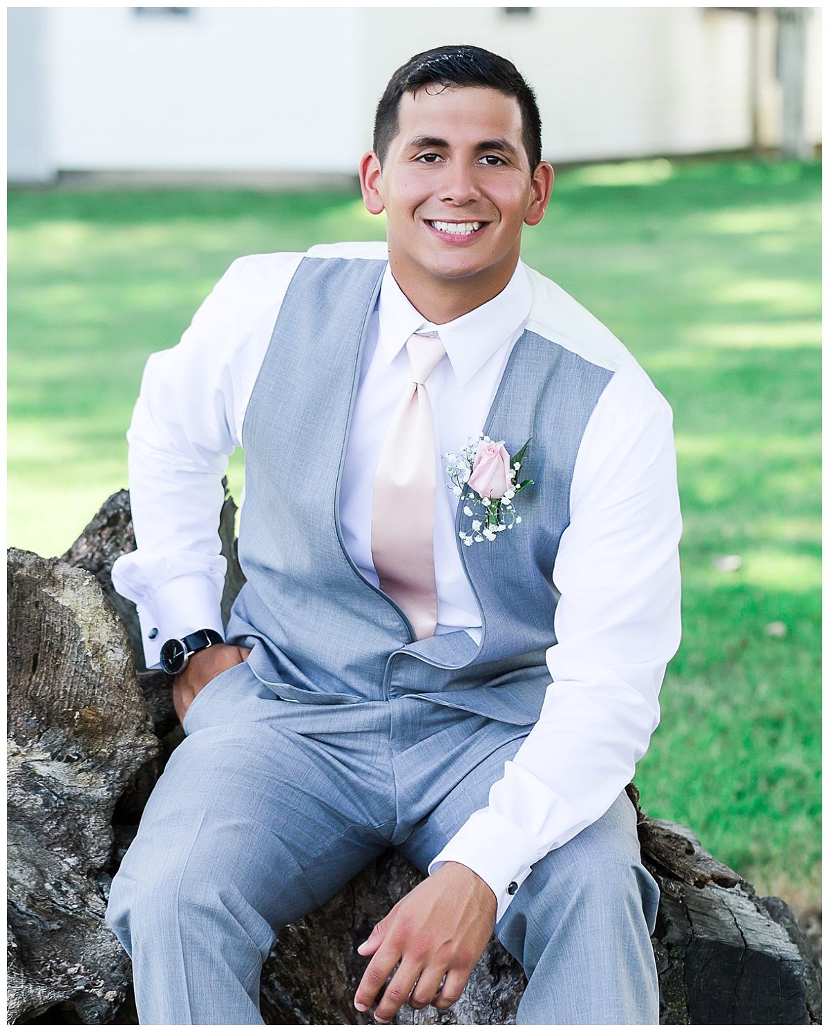 groom in gray tux pants and vest with pink boutonniere and tie sitting for portrait on his wedding day