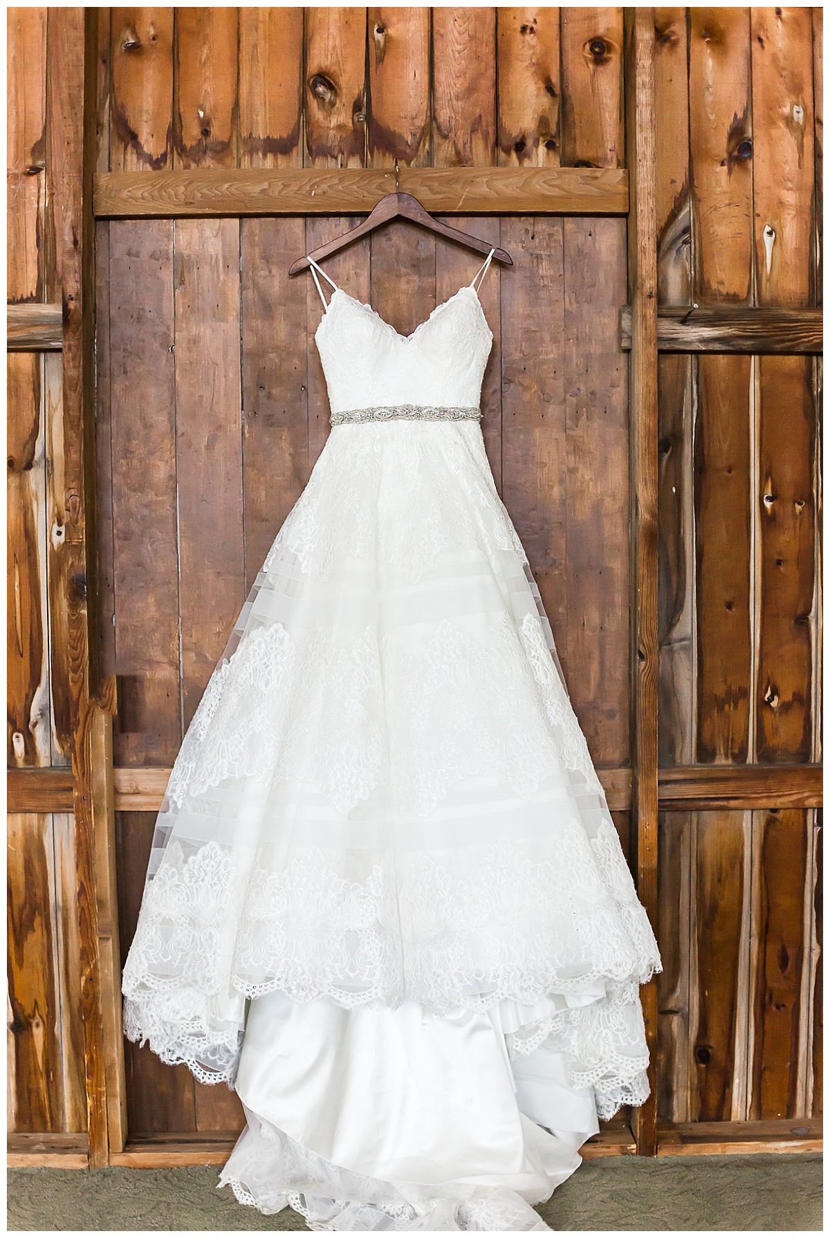 white ball gown style wedding dress hung in front of wooden background