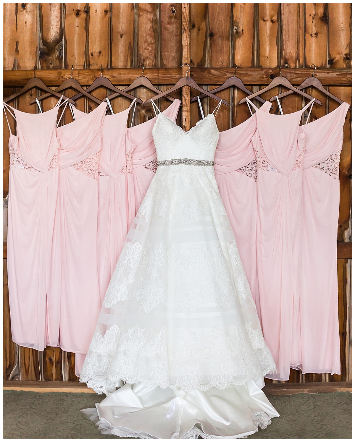 white ball gown style wedding dress hung with pink bridesmaids dresses with wooden background