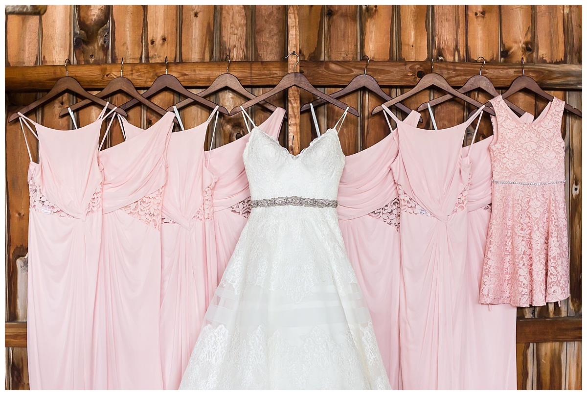 white ball gown style wedding dress hung with pink bridesmaids and flower girl dresses with wooden background