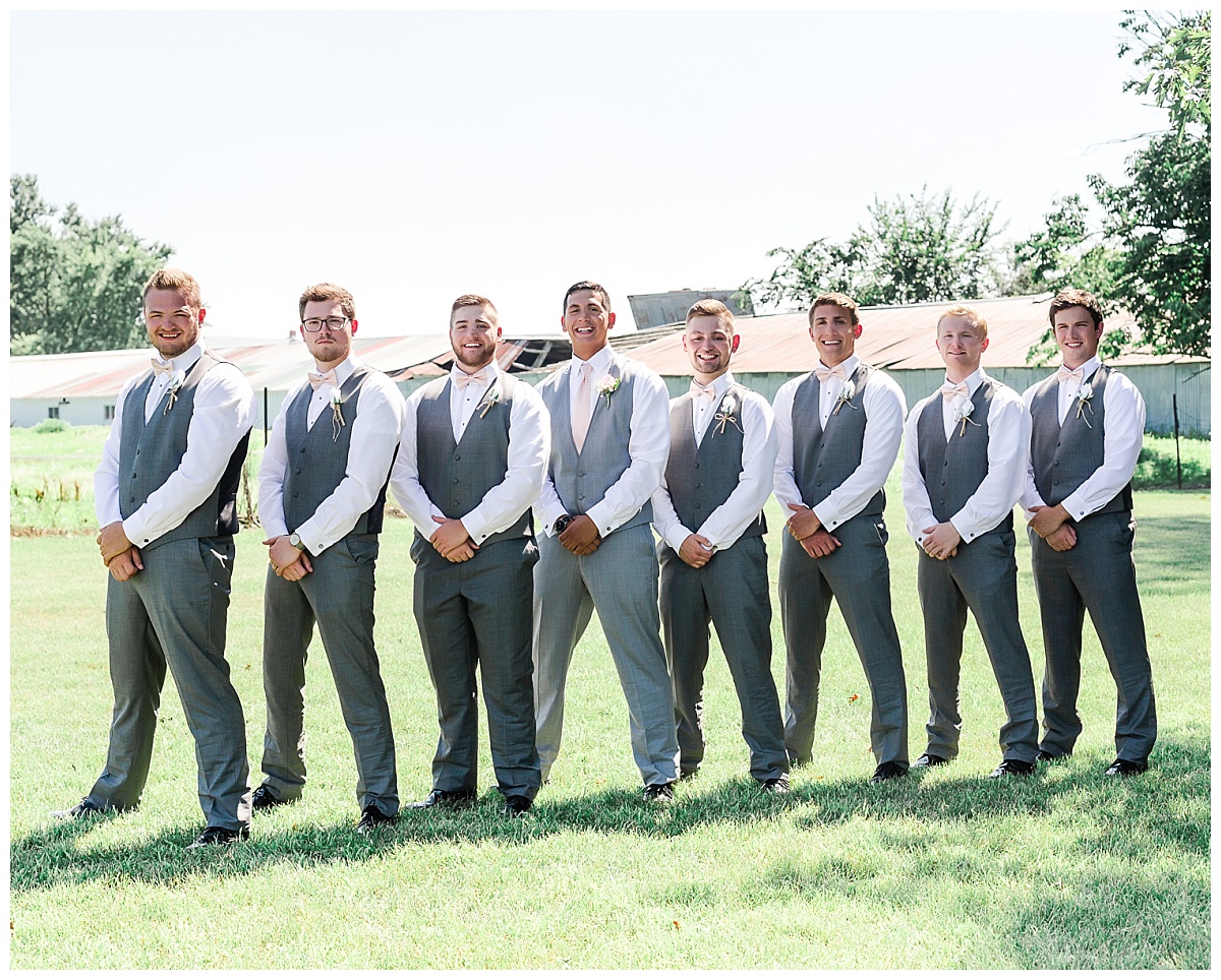 groomsmen wearing gray tux pants and vests standing facing same direction