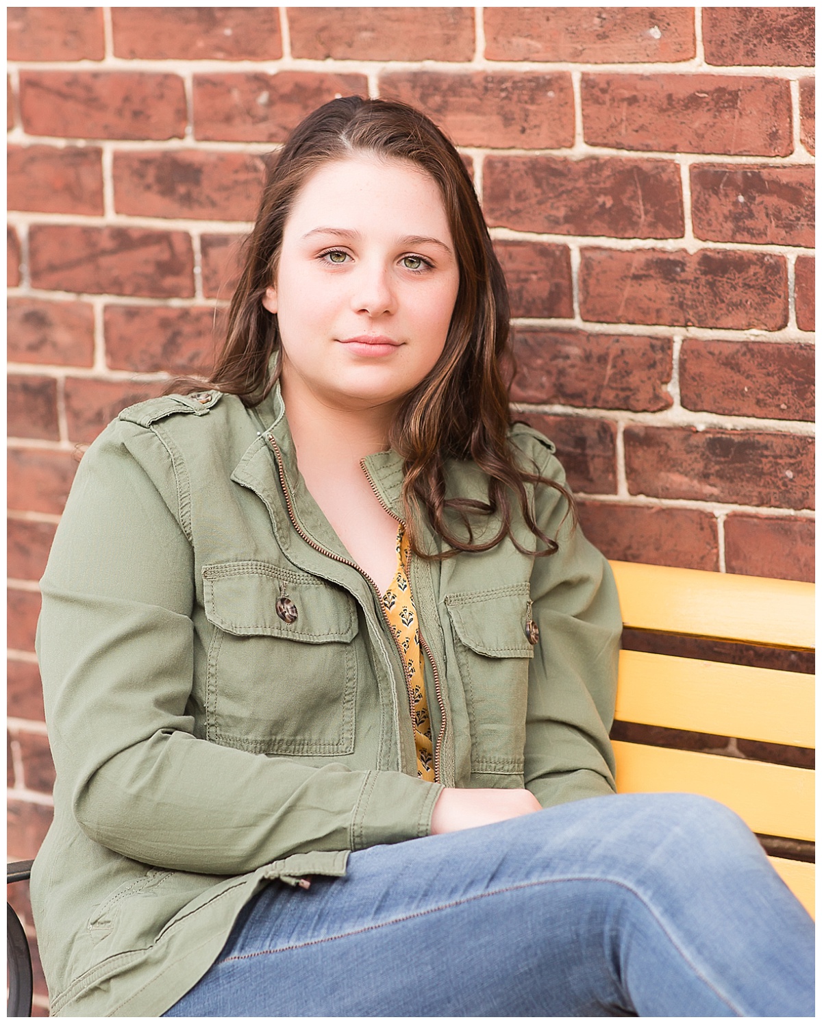 senior girl on bench with brick wall background